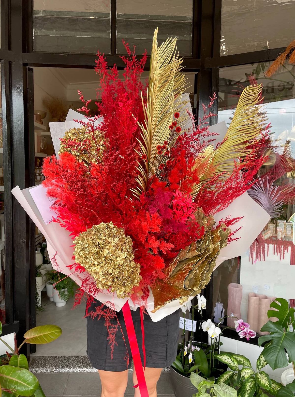 Bouquet of red and gold everlasting dried flowers for lunar chinese new year, with a person partially visible in the background.