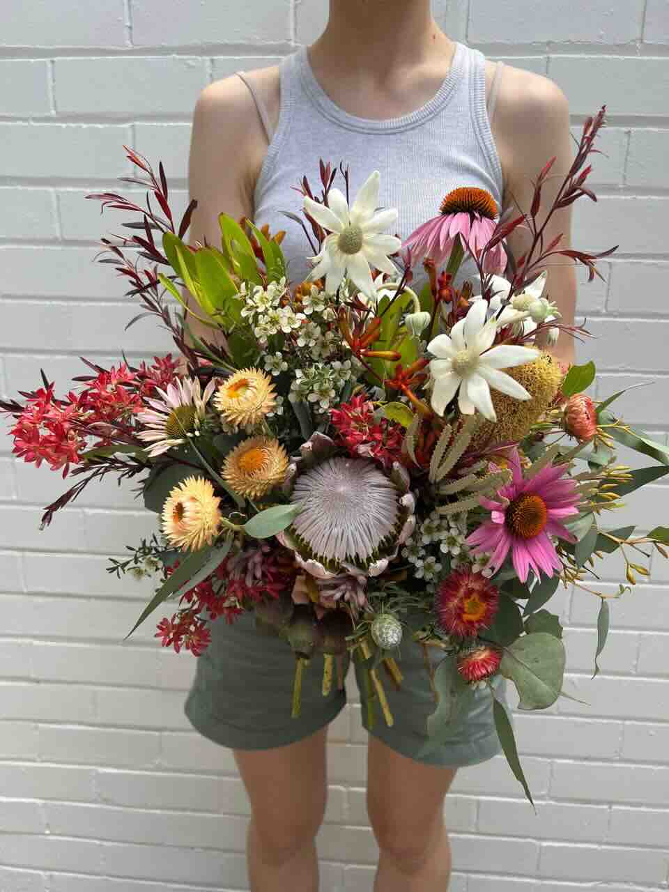 A fresh bouquet of Christmas flowers featuring a variety of colorful flowers such as red, white, and pink, held by a person against a brick wall background.