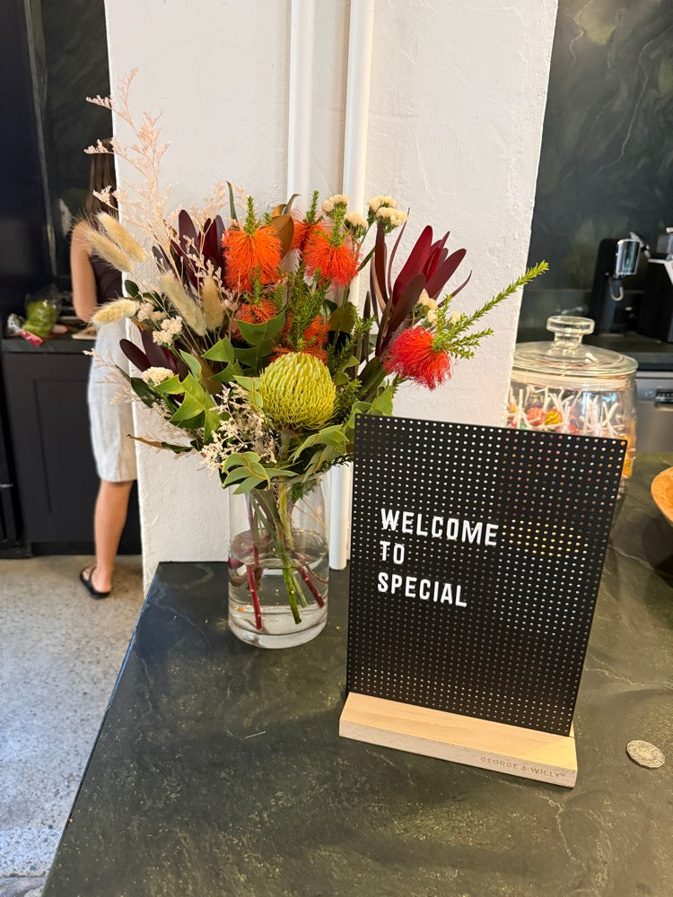 Vase of native flowers with a 'Welcome to Special' sign on a counter for weekly corporate office flower subscription entrance lobby area
