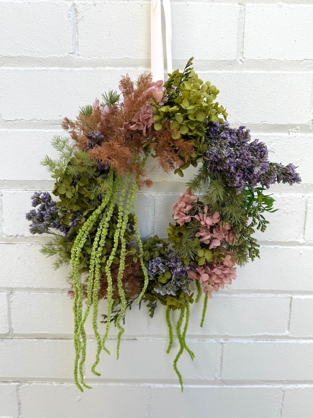 Decorative christmas wreath with greenery and flowers hanging on a white brick wall.